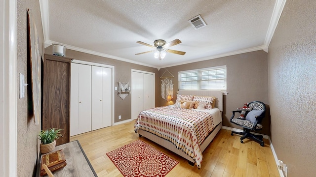 bedroom with visible vents, light wood finished floors, two closets, and a textured wall
