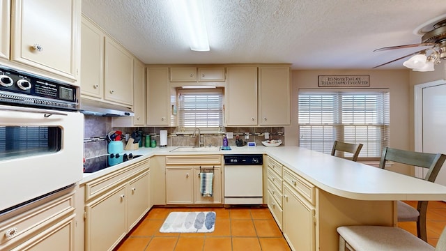 kitchen featuring white appliances, a peninsula, light countertops, a ceiling fan, and a sink
