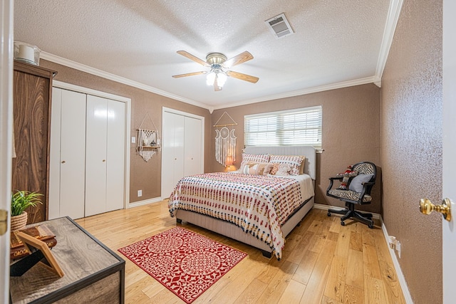 bedroom with ornamental molding, visible vents, light wood-type flooring, and two closets