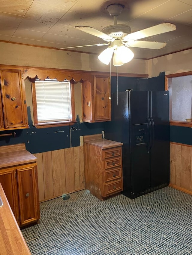 kitchen with black fridge with ice dispenser, ceiling fan, and wooden walls