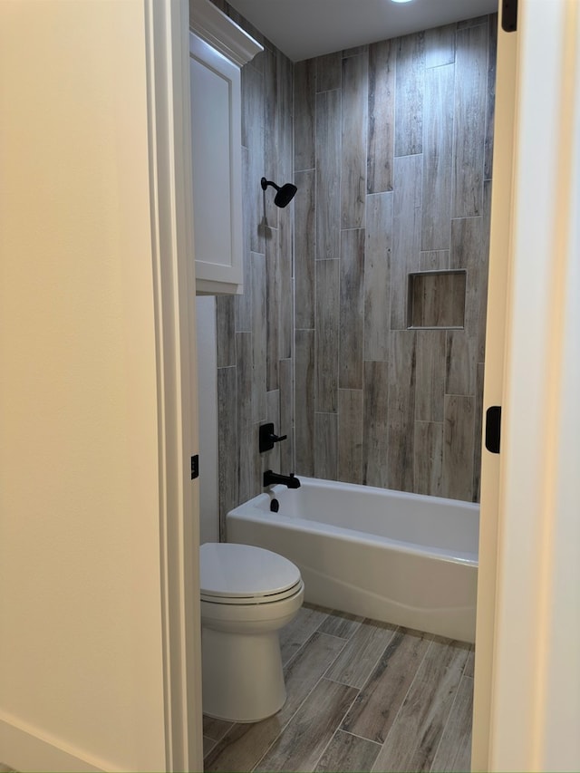 bathroom with hardwood / wood-style flooring, toilet, and tiled shower / bath