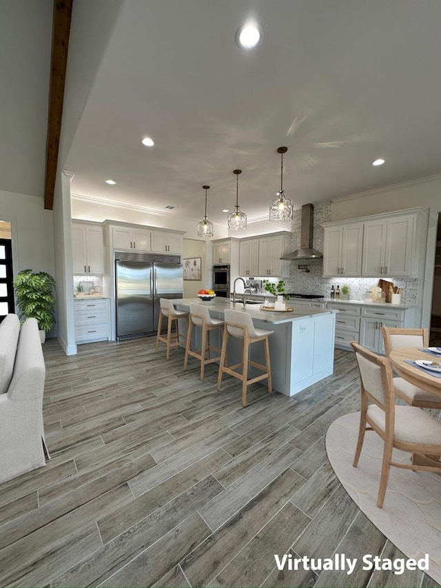 kitchen featuring pendant lighting, light countertops, white cabinetry, built in refrigerator, and wall chimney exhaust hood