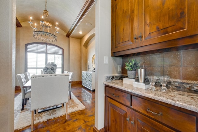 kitchen with light stone counters, a chandelier, dark hardwood / wood-style floors, decorative backsplash, and lofted ceiling