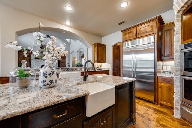 kitchen with appliances with stainless steel finishes, light stone counters, sink, light hardwood / wood-style flooring, and tasteful backsplash