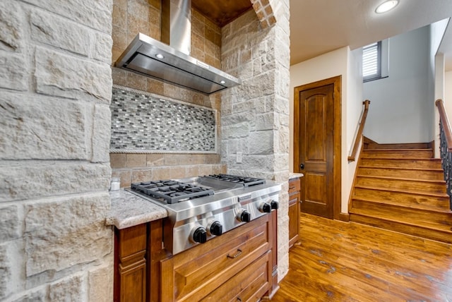 kitchen featuring light stone countertops, stainless steel gas stovetop, light hardwood / wood-style flooring, and wall chimney exhaust hood