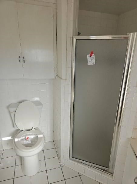 bathroom featuring tile patterned flooring, a shower with door, tile walls, and toilet