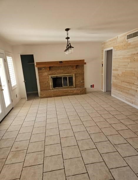 unfurnished living room featuring a notable chandelier, wood walls, and light tile patterned floors