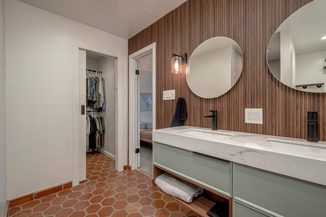 full bathroom with double vanity, tile patterned flooring, wood walls, a sink, and baseboards