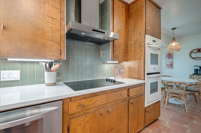 kitchen with wall chimney range hood, brown cabinets, white double oven, decorative backsplash, and stainless steel dishwasher
