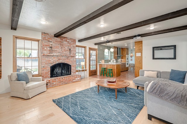 living room with a fireplace, a textured ceiling, beamed ceiling, and light wood-style flooring