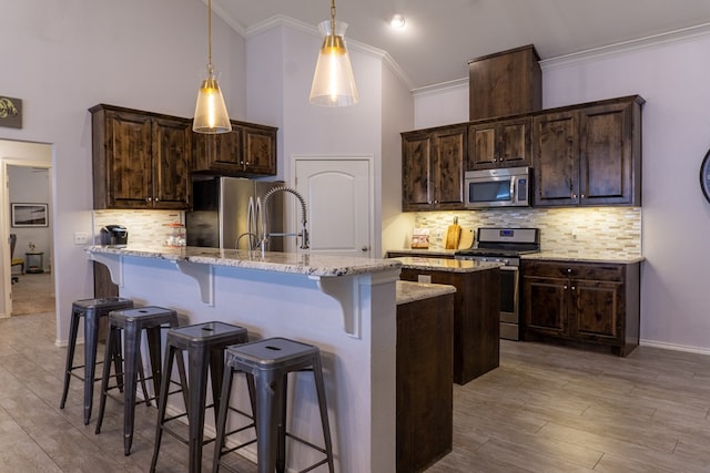 kitchen with light stone counters, dark brown cabinetry, stainless steel appliances, and a kitchen island with sink