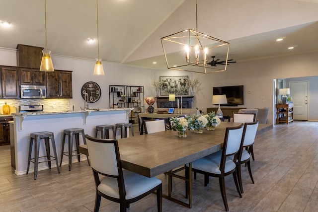 dining area featuring an inviting chandelier, crown molding, high vaulted ceiling, and light hardwood / wood-style flooring