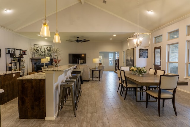 dining space featuring ceiling fan with notable chandelier, light wood-type flooring, crown molding, and high vaulted ceiling