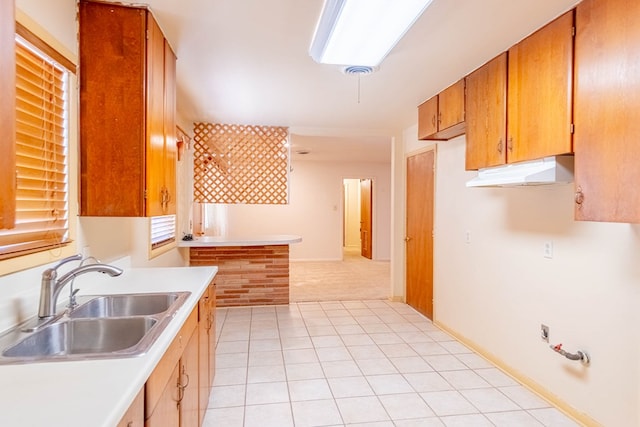 kitchen featuring visible vents, brown cabinets, under cabinet range hood, a sink, and light countertops