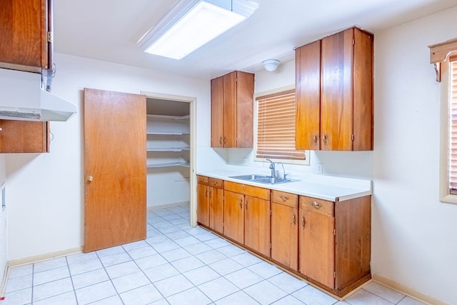 kitchen with light countertops, light tile patterned floors, brown cabinets, and a sink