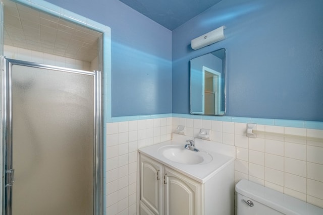 full bath with a wainscoted wall, toilet, tile walls, a shower stall, and vanity