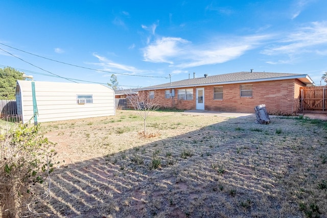 back of house featuring a patio, fence, an outdoor structure, a lawn, and brick siding