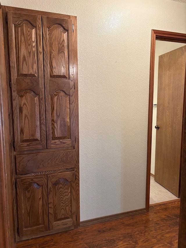 hallway featuring light wood finished floors, baseboards, and a textured wall