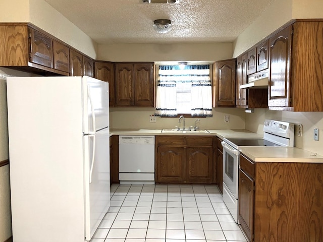 kitchen with under cabinet range hood, light countertops, light tile patterned flooring, white appliances, and a sink