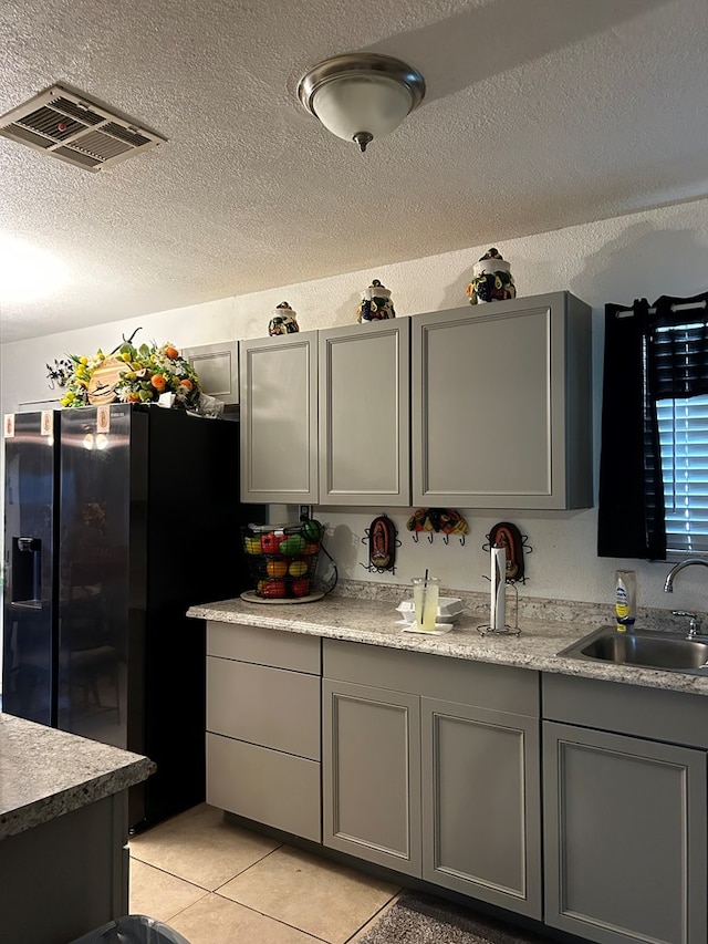 1202 N Gillis Ft, Stockton, TX 79735 - kitchen with gray cabinets, refrigerator with ice dispenser, light countertops, a textured ceiling, and light tile patterned floors