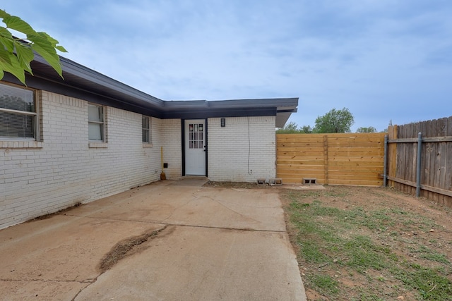 view of exterior entry with fence, brick siding, and a patio