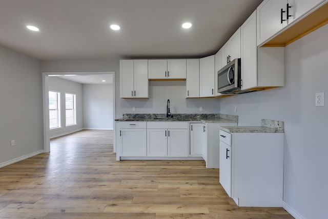 kitchen featuring stainless steel microwave, a sink, baseboards, recessed lighting, and light wood-style floors