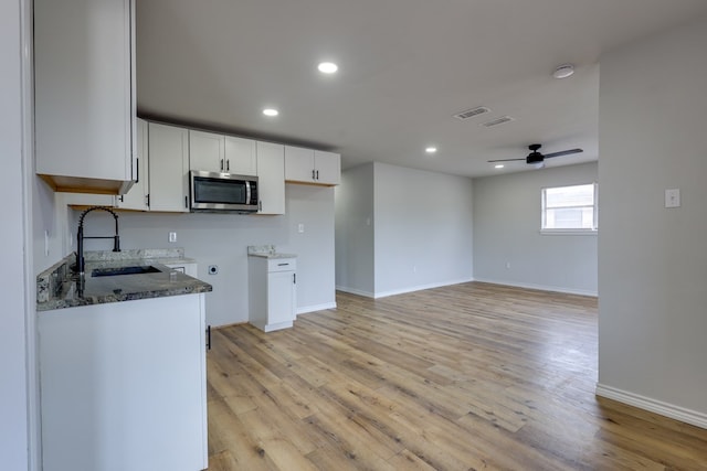 kitchen with stainless steel microwave, a sink, dark stone counters, light wood-style floors, and baseboards