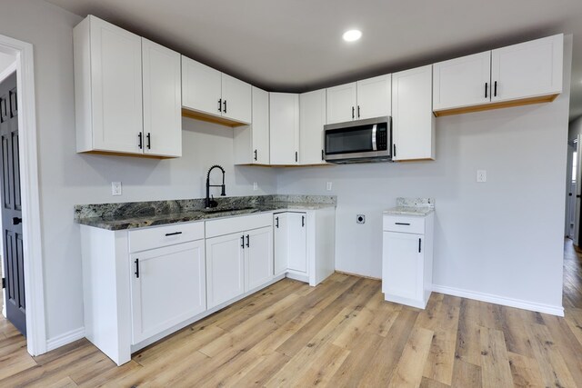kitchen with stainless steel microwave, a sink, dark stone counters, light wood finished floors, and white cabinets