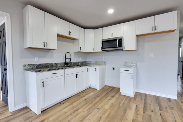 kitchen with stainless steel microwave, a sink, dark stone counters, light wood finished floors, and white cabinets