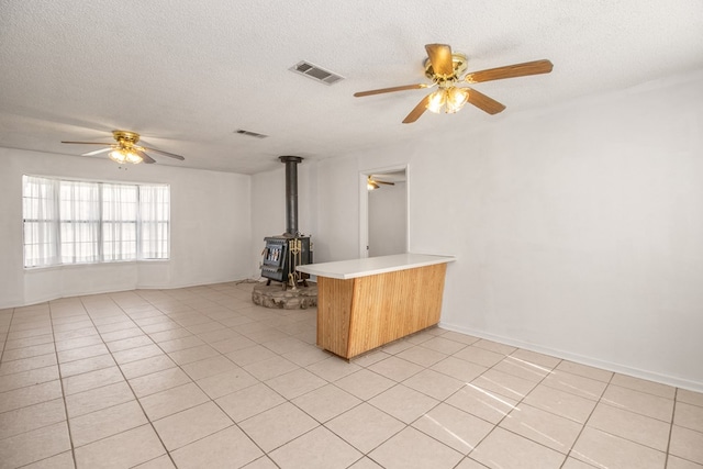 unfurnished living room featuring ceiling fan, light tile patterned floors, a wood stove, and a textured ceiling