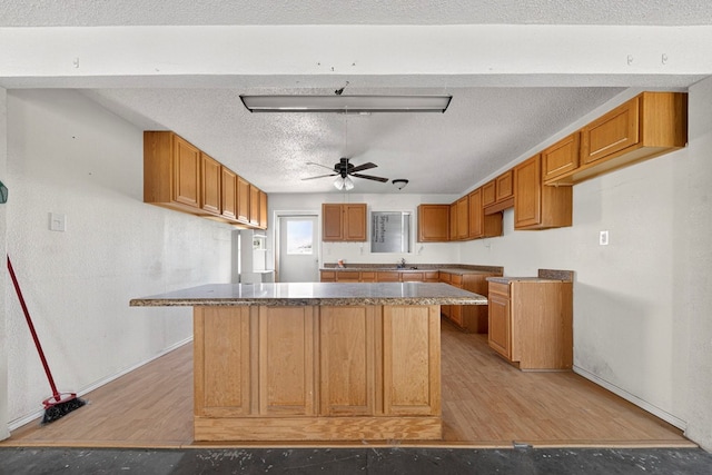 5408 E Loop 250e Unit A, Midland, TX 79705 - kitchen with ceiling fan, a kitchen island, brown cabinetry, light wood-type flooring, and a textured ceiling
