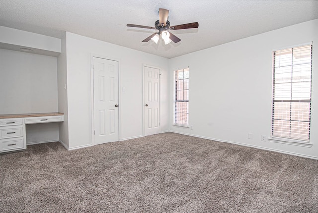 unfurnished bedroom featuring multiple closets, multiple windows, built in desk, and carpet