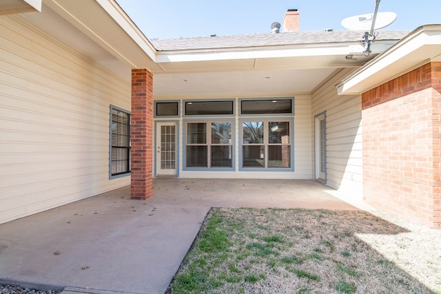 property entrance with brick siding, a chimney, and a patio