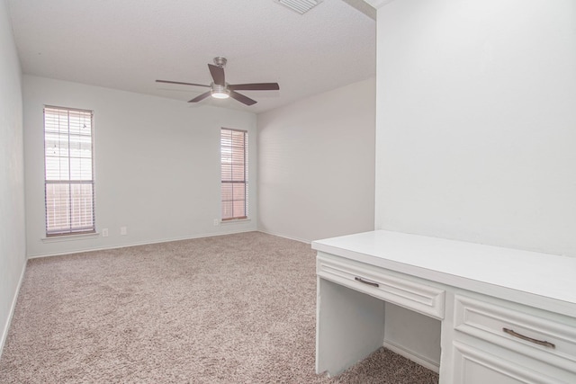 empty room with built in study area, carpet flooring, ceiling fan, and a wealth of natural light