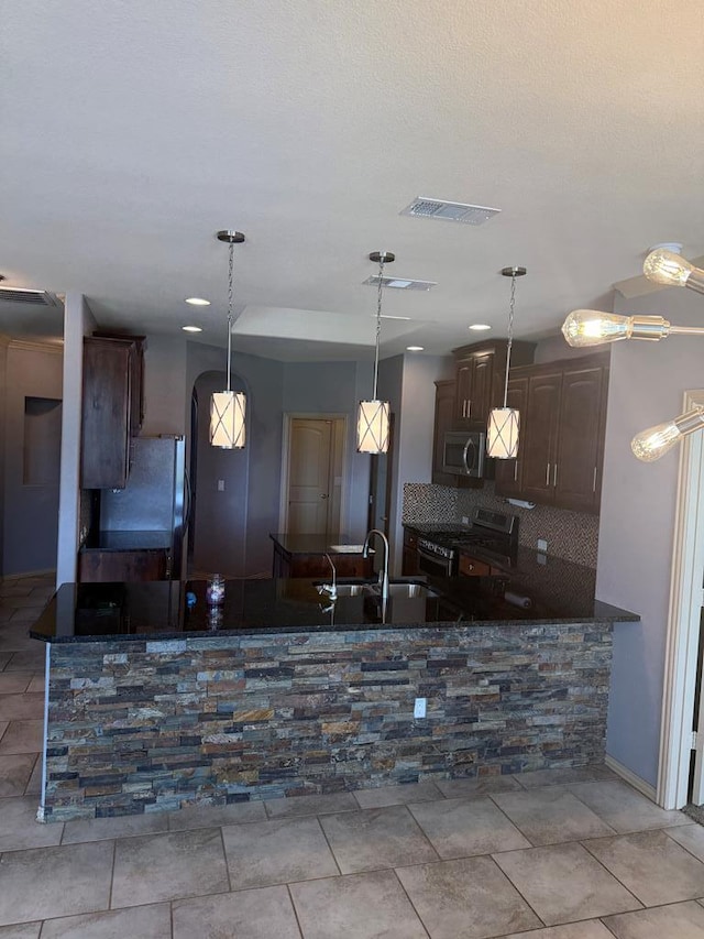 5702 San Miguel Ave, Midland, TX 79705 - kitchen featuring appliances with stainless steel finishes, backsplash, dark brown cabinetry, hanging light fixtures, and a peninsula