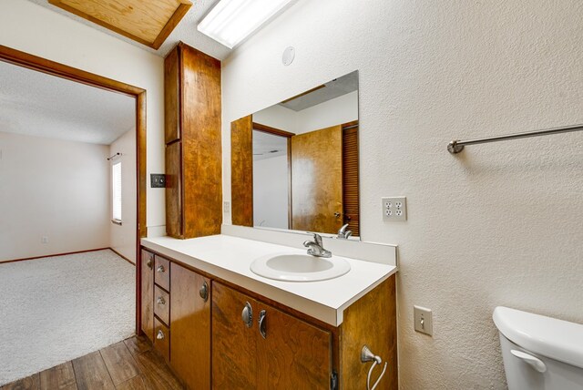 bathroom featuring toilet, vanity, a textured wall, and wood finished floors