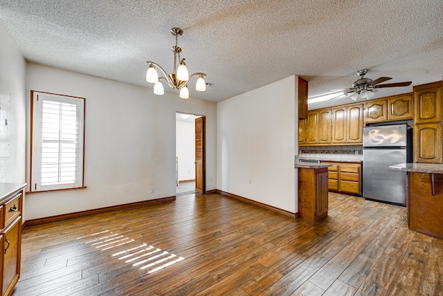 kitchen featuring ceiling fan with notable chandelier, a textured ceiling, decorative light fixtures, dark hardwood / wood-style flooring, and stainless steel refrigerator