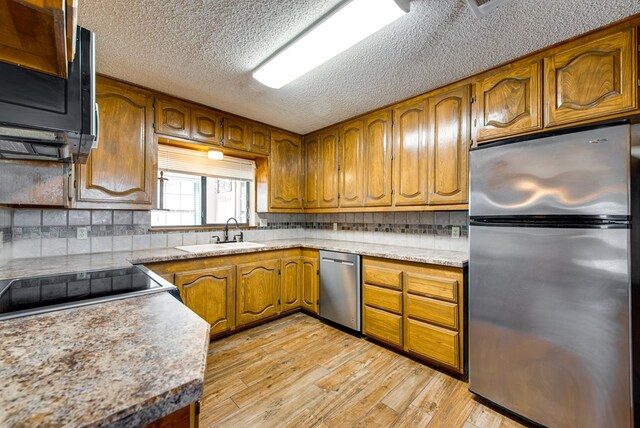 kitchen with tasteful backsplash, light wood-type flooring, appliances with stainless steel finishes, brown cabinetry, and a sink