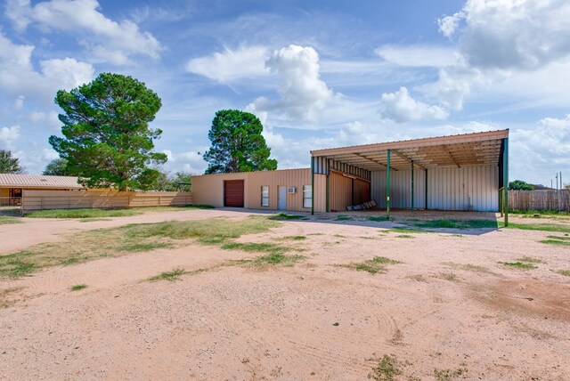 exterior space with dirt driveway, fence, a detached carport, an outdoor structure, and a pole building