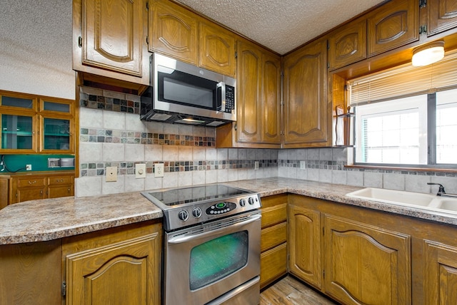 kitchen with appliances with stainless steel finishes, tasteful backsplash, a textured ceiling, sink, and light hardwood / wood-style floors