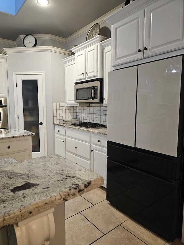 kitchen with light tile patterned flooring, ornamental molding, white cabinets, stainless steel appliances, and backsplash