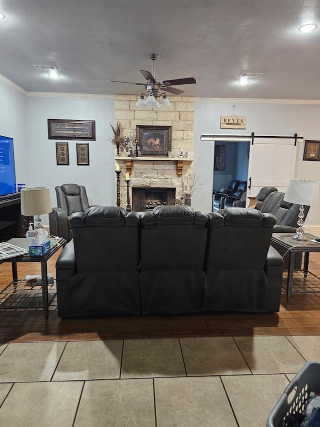 living room featuring a fireplace, ornamental molding, ceiling fan, a barn door, and a textured ceiling