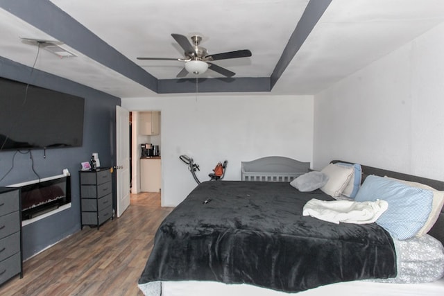 bedroom featuring a tray ceiling, wood finished floors, visible vents, and ceiling fan