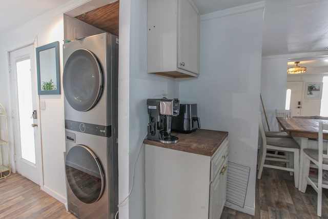 laundry area featuring laundry area, wood finished floors, ornamental molding, and stacked washing maching and dryer