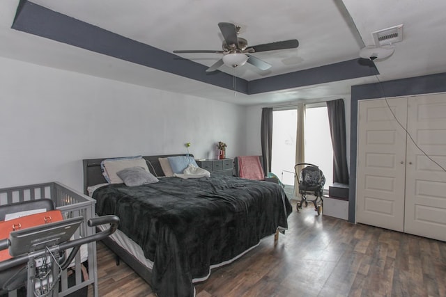 bedroom featuring a tray ceiling, wood finished floors, visible vents, and ceiling fan