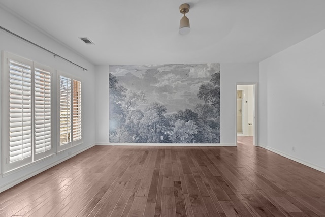 empty room featuring an accent wall, visible vents, baseboards, and wood finished floors