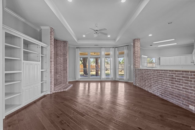 unfurnished living room with brick wall, a tray ceiling, wood finished floors, and crown molding