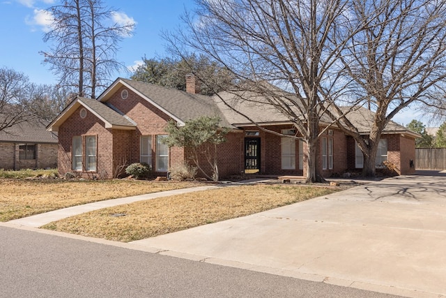 ranch-style home featuring a shingled roof, a front yard, brick siding, and a chimney