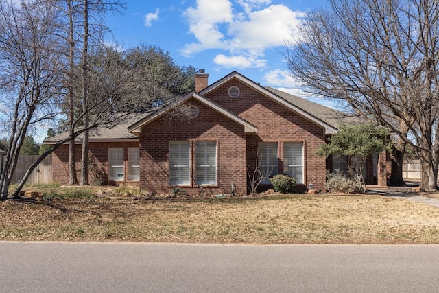 ranch-style home with roof with shingles, brick siding, a chimney, and a front yard