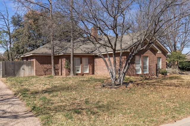 ranch-style house featuring brick siding, fence, a chimney, and a front lawn